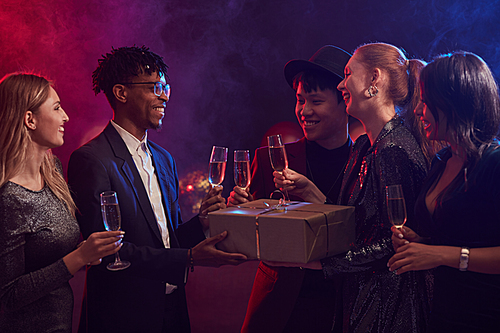 Multi-ethnic group of elegant young people exchanging presents during party in smoky night club