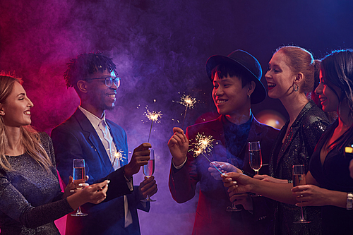 Multi-ethnic group of elegant young people lighting sparklers during Christmas party in smoky night club