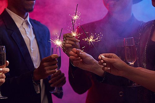 Closeup of young people lighting sparklers while enjoying Christmas party in smoky night club, copy space