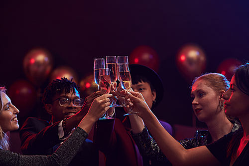 Group of elegant young people raising champagne glasses while enjoying party in nightclub, copy space