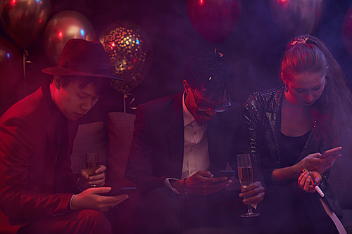 Group of trendy young people using smartphones during party in smoky nightclub, copy space