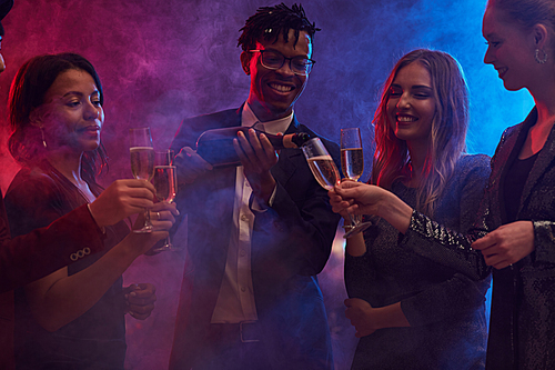 Group of cheerful young people pouring champagne in smoky nightclub while enjoying party