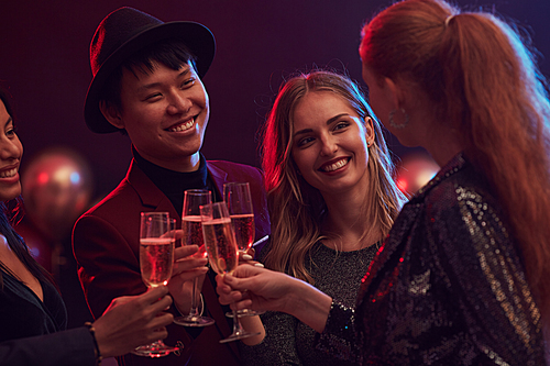 Multi-ethnic group of people clinking champagne glasses while enjoying party in nightclub or restaurant, copy space