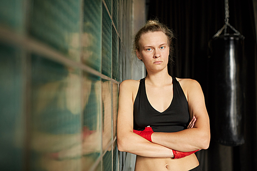 Waist up portrait of tough sportswoman  while leaning on glass wall in sports club, copy space