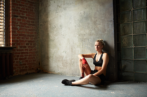 Dramatic wide angle portrait of tough sportswoman sitting by concrete wall, copy space
