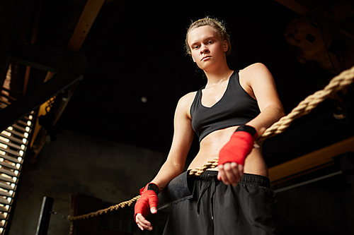 Dramatic low angle portrait of tough female boxer looking down at camera while standing in boxing ring, copy space