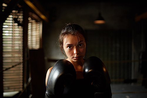 Dramatic portrait of young woman  with determination during boxing practice in dark room, copy space