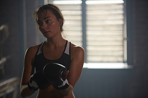 Dark toned portrait of sweaty young woman practicing boxing in sports club, copy space