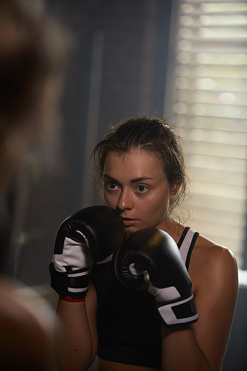 Candid portrait of female fighter hitting punching bag at boxing practice, copy space
