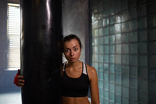 Candid waist up portrait of tough female fighter posing with punching bag at boxing practice, copy space