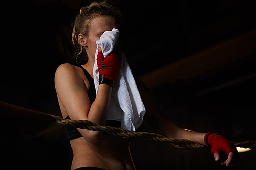 Dark toned portrait of tough sportswoman wiping sweat with towel after practice, copy space