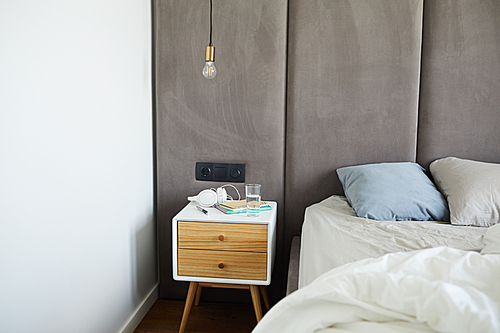 Part of bed with white blanket and grey pillows with nightstand near by with group of objects