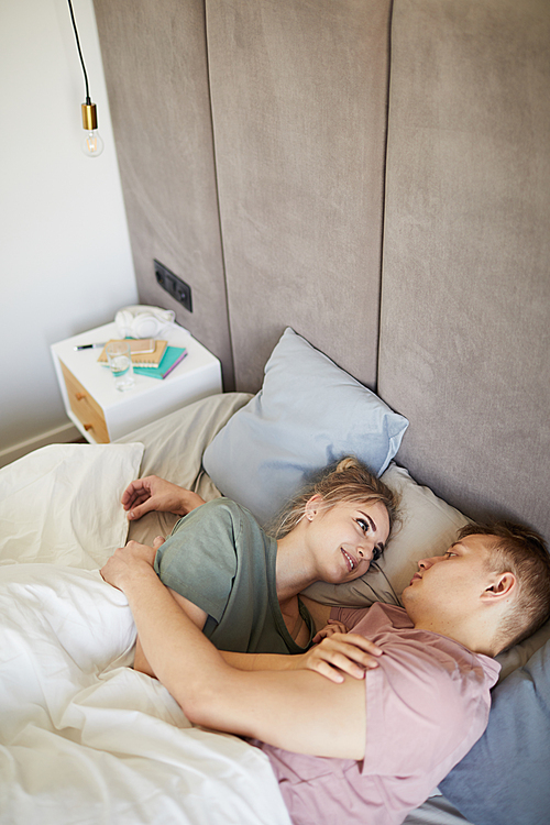 Happy young amorous spouses looking at one another while lying in bed