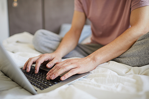 Hands of young man over laptop keypad during network on bed in the morning