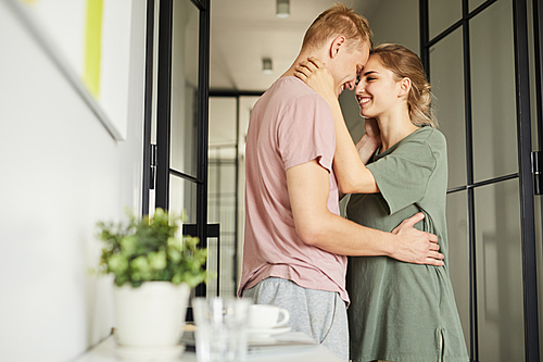 Happy young husband and wife standing in embrace by the door of bedroom at home