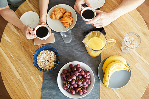 Fresh food and snacks on served table and hands of young couple with cups of coffee over it