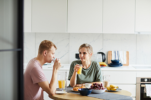 Young woman and her husband drinking orange juice by breakfast in the morning