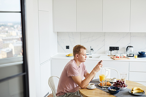 Young man in casualwear texting in smartphone by served table while having brunch