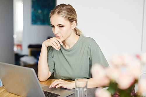 Young female freelancer in casualwear looking at laptop display during network at home