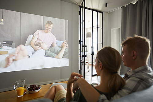 Young amorous couple watching their home video while sitting in living-room in front of plasma tv set