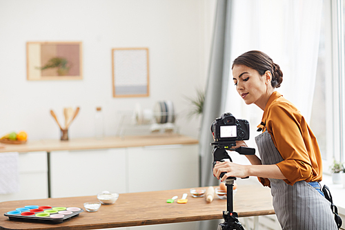 Waist up portrait of beautiful young woman setting up camera while filming cooking tutorial in studio, copy space