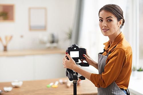 Waist up portrait of beautiful woman setting up camera and smiling while filming cooking tutorial in studio, copy space