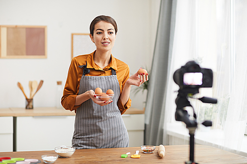 Waist up portrait of beautiful young woman talking to camera while filming baking tutorial in studio, copy space