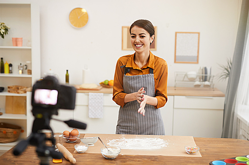 Waist up portrait of beautiful young woman smiling at camera while filming baking tutorial in studio, copy space