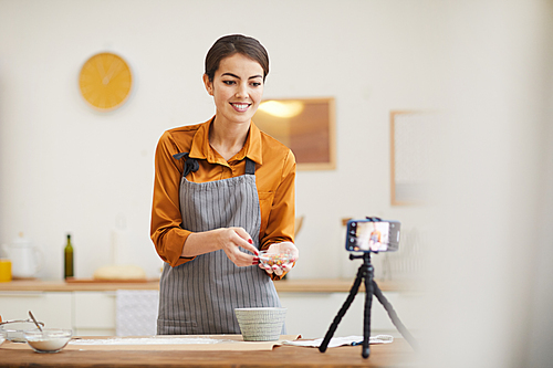 Waist up portrait of beautiful young woman smiling at camera while filming baking tutorial for video channel, copy space