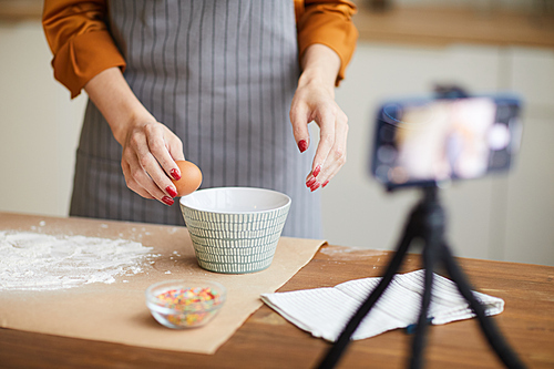 Cropped portrait of unrecognizable young woman breaking eggs while filming baking tutorial for video channel, copy space