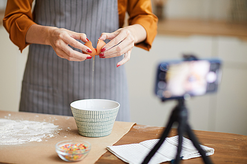 Close up of unrecognizable young woman breaking eggs while filming baking tutorial for video channel, copy space