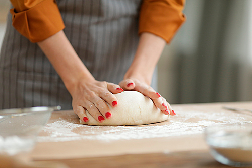 Closeup of unrecognizable woman kneading batter while baking homemade pastry on kitchen table, copy space