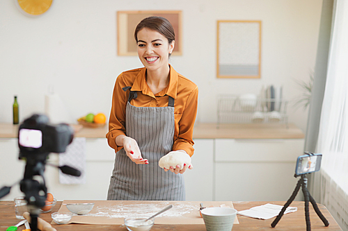 Portrait of beautiful young woman holding fresh batter and smiling at camera while filming baking tutorial for video channel, copy space