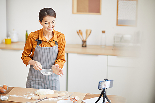 Waist up portrait of beautiful young woman smiling at camera while filming baking tutorial for video channel, copy space