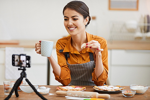 Portrait of beautiful young woman smiling at camera while filming baking tutorial for video channel, copy space