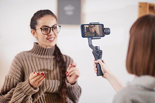 Portrait of unrecognizable woman holding smartphone on stabilizing monopod while recording video vlog for beauty and lifestyle channel