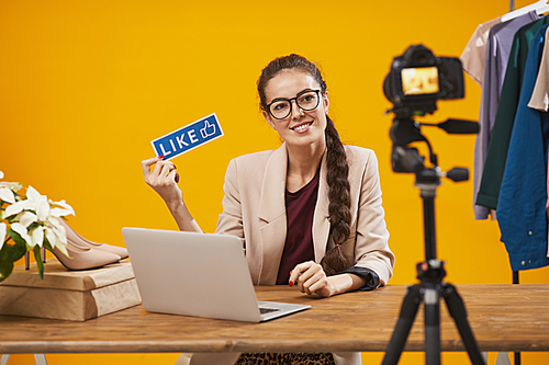 Portrait of contemporary young woman holding Like and Subscribe word and smiling at camera while filming video for beauty and lifestyle channel, copy space