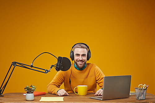 Horizontal studio portrait of young adult man working as radio presenter sitting at table in his workplace
