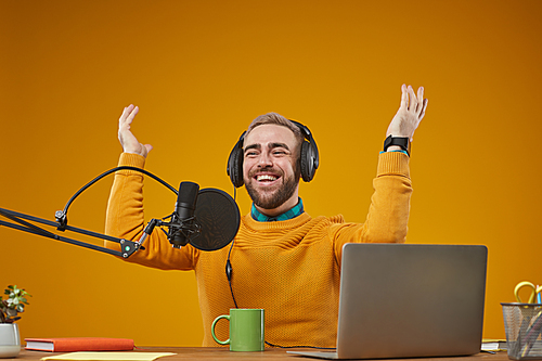 Horizontal studio portrait of emotional radio presenter wearing stylish casual clothes sitting at desk recording broadcast