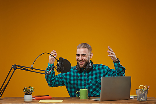 Horizontal studio shot of cheerful young radio presenter wearing stylish checked shirt enjoying his work