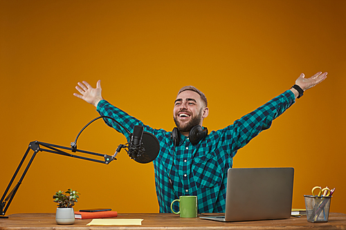 Horizontal studio shot of cheerful young man wearing checked shirt finishing live stream show recording