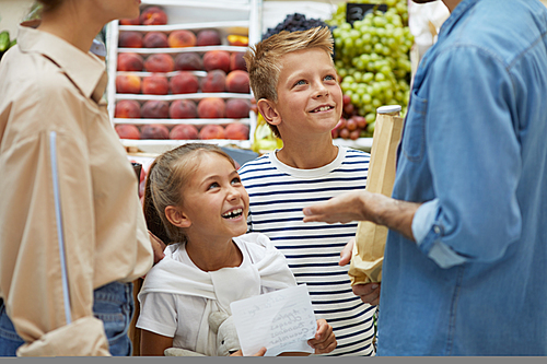 Portrait of two happy children enjoying shopping at farmers market with parents, copy space