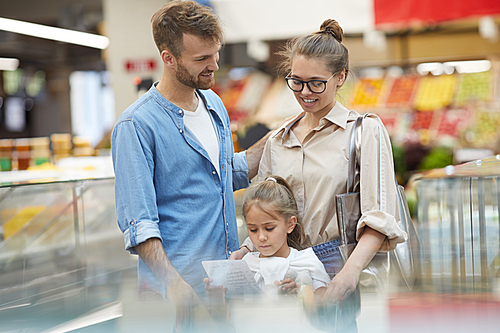 Portrait of happy young family grocery shopping together at supermarket, copy space