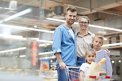 Portrait of contemporary young family posing in supermarket while enjoying grocery shopping, copy space