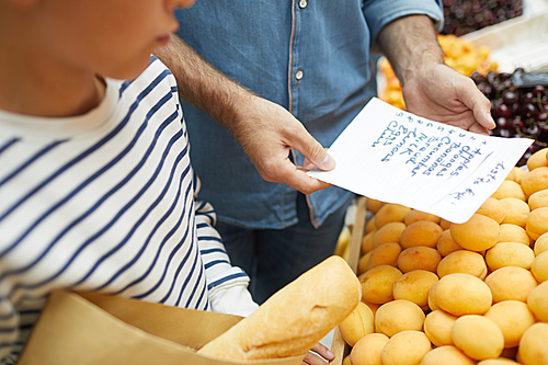 High angle closeup of father reading shopping list while buying groceries at farmers market, copy space