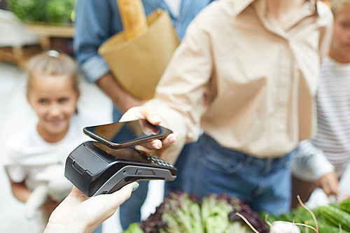 Closeup of young woman paying via smartphone at supermarket while shopping with family, copy space