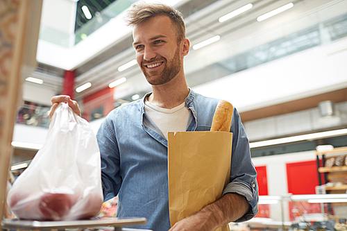 Waist up portrait of handsome young man weighing vegetables in supermarket and smiling at cashier, copy space