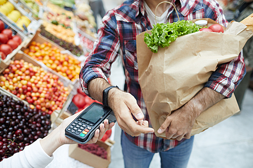 Closeup of unrecognizable man paying via smartwatch while grocery shopping at farmers market, copy space