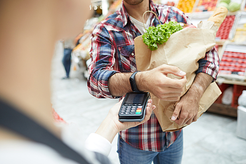 Close up of unrecognizable man paying via smartwatch while grocery shopping at farmers market, copy space