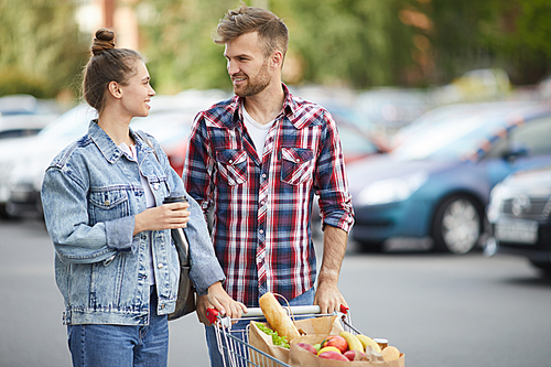Waist up portrait of contemporary young couple pushing shopping cart in parking lot after buying groceries, copy space